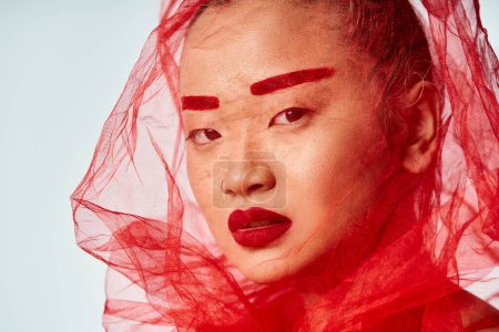 Asian woman with red makeup and veil posing gracefully.