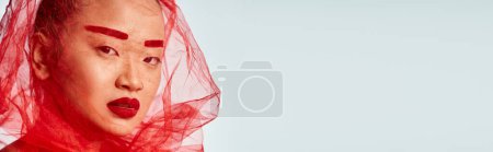 Foto de Una atractiva asiática posa graciosamente con un velo en la cabeza, vistiendo ropa vibrante. - Imagen libre de derechos