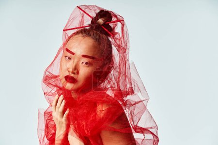 Asian woman exudes elegance in vibrant red dress and flowing veil.
