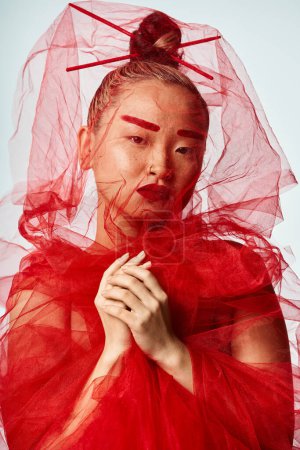 Asian woman exudes grace in red dress with a veil.
