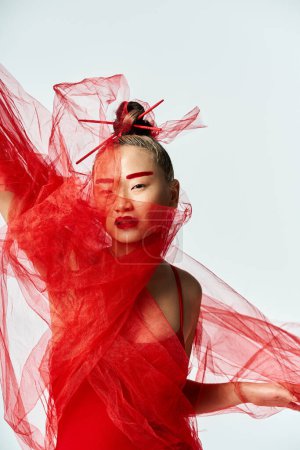 Foto de A vibrant Asian woman in a red dress poses gracefully wearing a veil. - Imagen libre de derechos