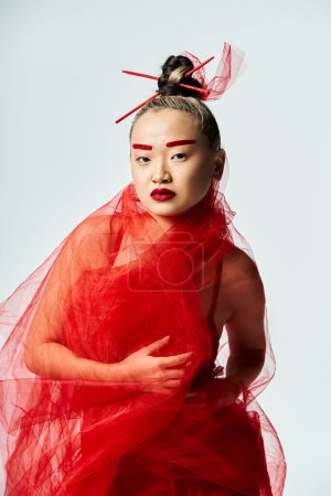 Asian woman in a striking red dress and veil poses gracefully.
