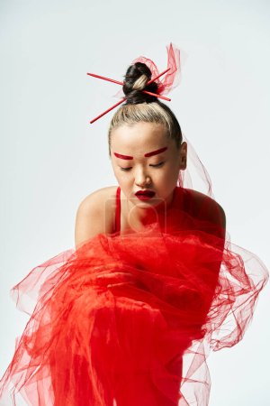 Faisant appel femme asiatique frappe une pose gracieuse dans une robe rouge dynamique et voile.