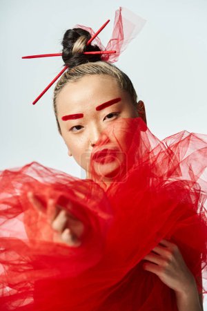 An attractive Asian woman in a vibrant red dress and matching makeup poses dynamically.