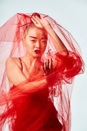 An attractive Asian woman poses in a vibrant red dress and a veil over her head.