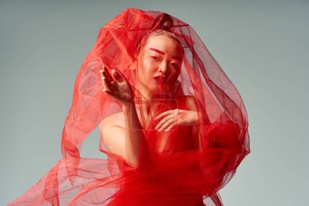 Mujer asiática posa elegantemente en vestido rojo y velo.