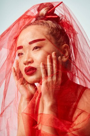 Foto de Asian woman poses confidently in vibrant clothes, wearing a red lipstick and a veil. - Imagen libre de derechos
