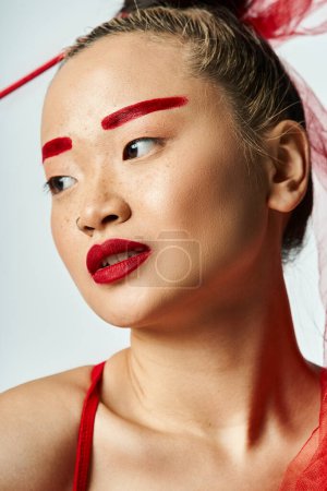 Asiatin posiert in leuchtenden Kleidern, trägt Schleier und kräftigen roten Lippenstift.