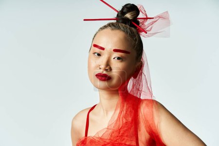 Une jolie femme asiatique avec un maquillage rouge vibrant et un voile sur sa tête pose gracieusement.