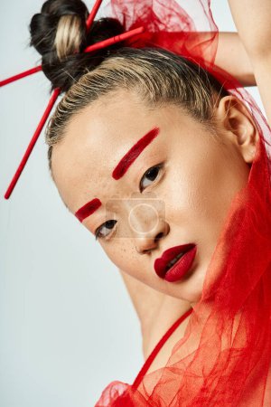 Une jolie femme asiatique en vêtements vibrants, portant un maquillage rouge et un voile rouge sur la tête.