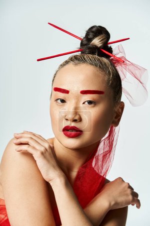 Asian woman in vibrant red makeup and a veil poses artistically.