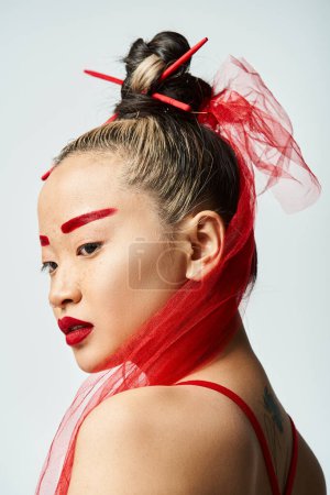 Asian woman poses with vibrant red makeup and veil.