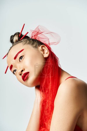 Enchanting Asian woman with red makeup and hair poses vibrantly.
