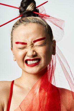 Foto de Una atractiva asiática con maquillaje rojo y un velo en la cabeza posa con gracia. - Imagen libre de derechos