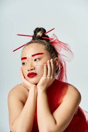 Asian woman in red dress, hands on face, exuding grace and emotion.
