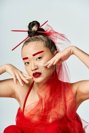 A captivating Asian woman in a vibrant red dress, hands on head.