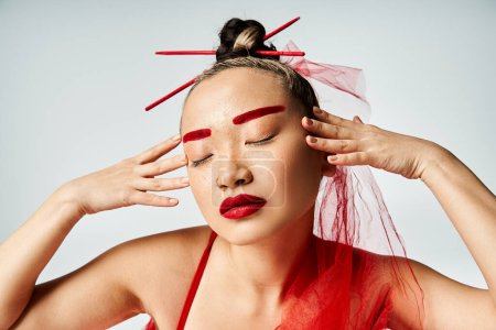Asian woman in vibrant red dress gracefully poses with eyes closed.