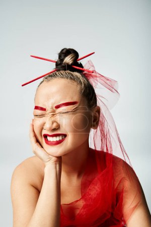 Femme asiatique avec maquillage rouge et voile de tête posant gracieusement.
