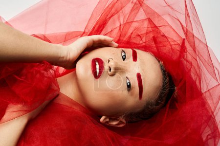 A vibrant Asian woman poses in a striking red dress and matching makeup.