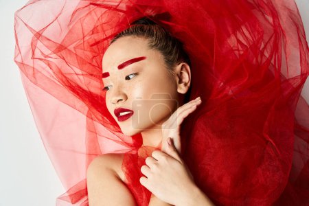 Photo for An attractive Asian woman in a vibrant red dress with a veil on her head poses gracefully. - Royalty Free Image