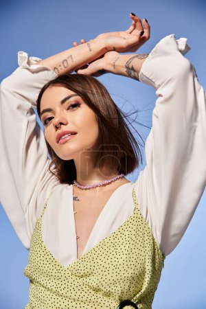 A young woman with brunette hair confidently displays a stylish tattoo on her arm in a studio setting.