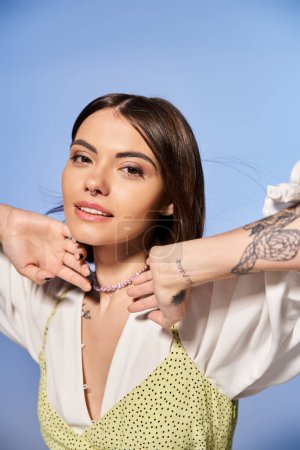 A young woman with brunette hair showcases her intricate arm tattoo in a studio setting.