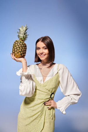Photo for A young woman with brunette hair joyfully holds a pineapple up to her face in a studio setting. - Royalty Free Image