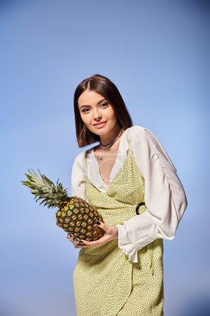 Photo for A stylish brunette woman in a dress, gracefully holding a vibrant pineapple. - Royalty Free Image