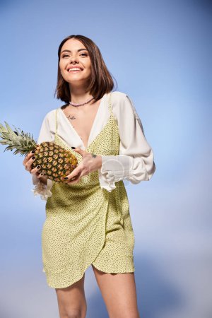 Eine brünette Frau hält anmutig eine lebendige Ananas in einem stilvollen Kleid.