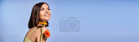 Photo for Young brunette woman elegantly placing a delicate flower in her hair in a serene studio setting. - Royalty Free Image