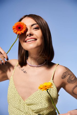 A young woman with brunette hair gracefully holds a vibrant flower in her hand.
