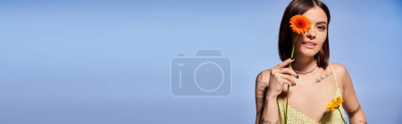 Téléchargez les photos : Une jeune femme aux cheveux bruns est ornée d'une fleur délicate dans un cadre de studio serein. - en image libre de droit