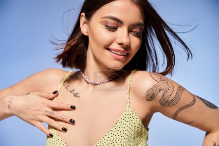 A young woman with brunette hair proudly showing off a tattoo on her arm in a studio setting.