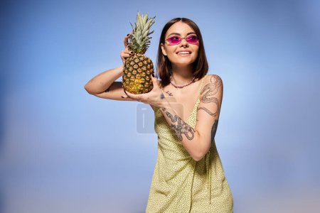Téléchargez les photos : Une jeune femme aux cheveux bruns pose élégamment dans une robe jaune vif, tenant un ananas frais. - en image libre de droit