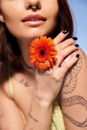 Une jeune femme aux cheveux bruns tient doucement une fleur délicate dans sa main, exsudant élégance et grâce.