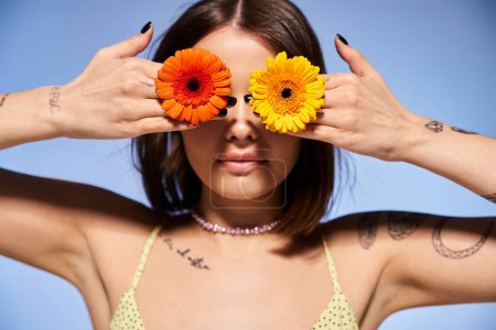 Téléchargez les photos : Une jeune femme aux cheveux bruns tenant deux fleurs devant ses yeux dans un décor de studio. - en image libre de droit