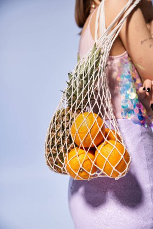Una mujer joven con el pelo moreno felizmente sostiene una bolsa llena de naranjas frescas en un ambiente de estudio vibrante.