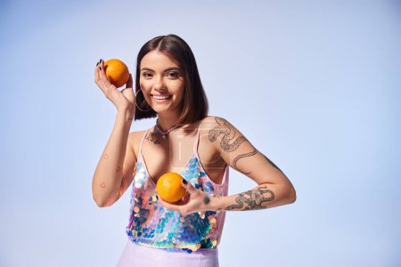 Une jeune femme aux cheveux bruns tient délicatement deux oranges vibrantes dans ses mains dans un décor de studio.