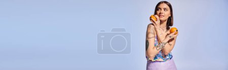 Téléchargez les photos : Une femme brune tatouée tient joyeusement deux oranges vibrantes dans ses mains. - en image libre de droit
