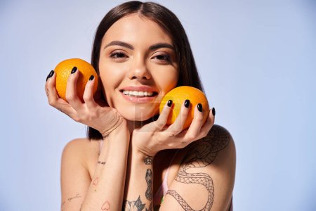 Une jeune femme aux cheveux bruns tenant ludique deux oranges devant son visage dans un décor de studio.