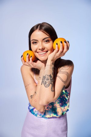 A young woman with brunette hair holds two oranges in front of her face in a studio setting.