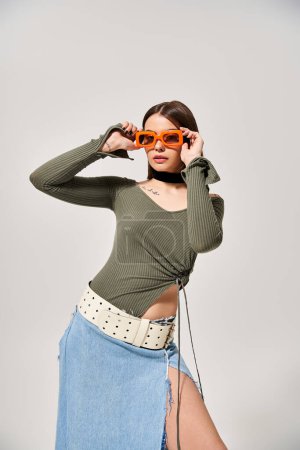 A stylish young woman with brunette hair in a skirt with a pair of sunglasses resting on her head.