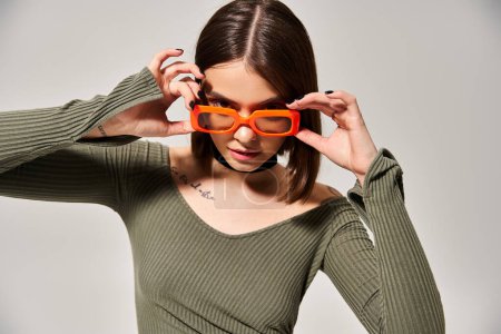 Brunette woman in a vibrant green shirt and trendy orange glasses poses confidently in a studio setting.