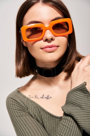 Une femme brune respire le style et la confiance tout en portant des lunettes de soleil orange tendance dans un cadre studio.
