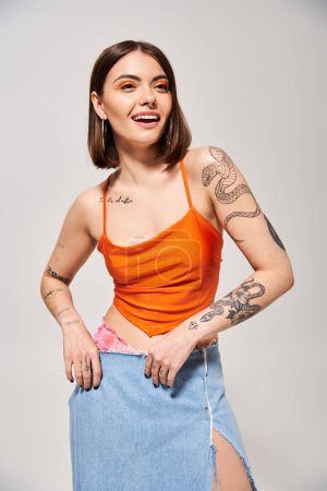 A brunette woman wearing a skirt confidently displaying a tattoo on her arm in a studio setting.