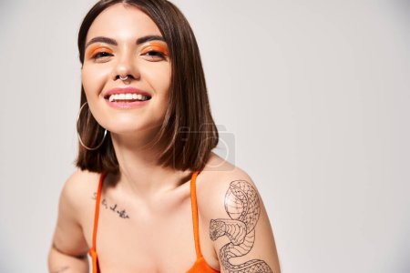 Eine stylische junge Frau mit brünetten Haaren, die in einem Studio ein wunderschönes Tattoo auf ihrem Arm zeigt.