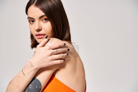A young woman with brunette hair showcasing a tattoo on her arm in a studio setting.