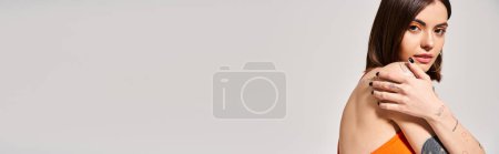 Téléchargez les photos : Une jeune femme aux cheveux bruns pose gracieusement en haut orange et gris élégant pour une séance photo en studio. - en image libre de droit