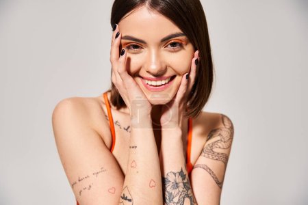 Eine junge Frau mit brünetten Haaren posiert im Studio, um ihre Tattoos zur Schau zu stellen.