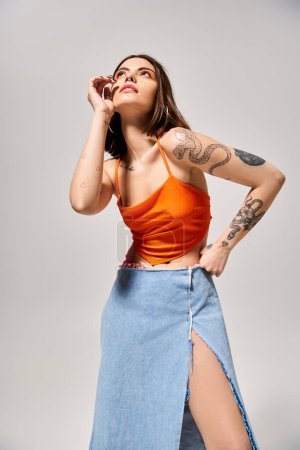 Téléchargez les photos : Une jeune femme aux cheveux bruns danse gracieusement dans une jupe bleue vibrante et un haut orange. - en image libre de droit